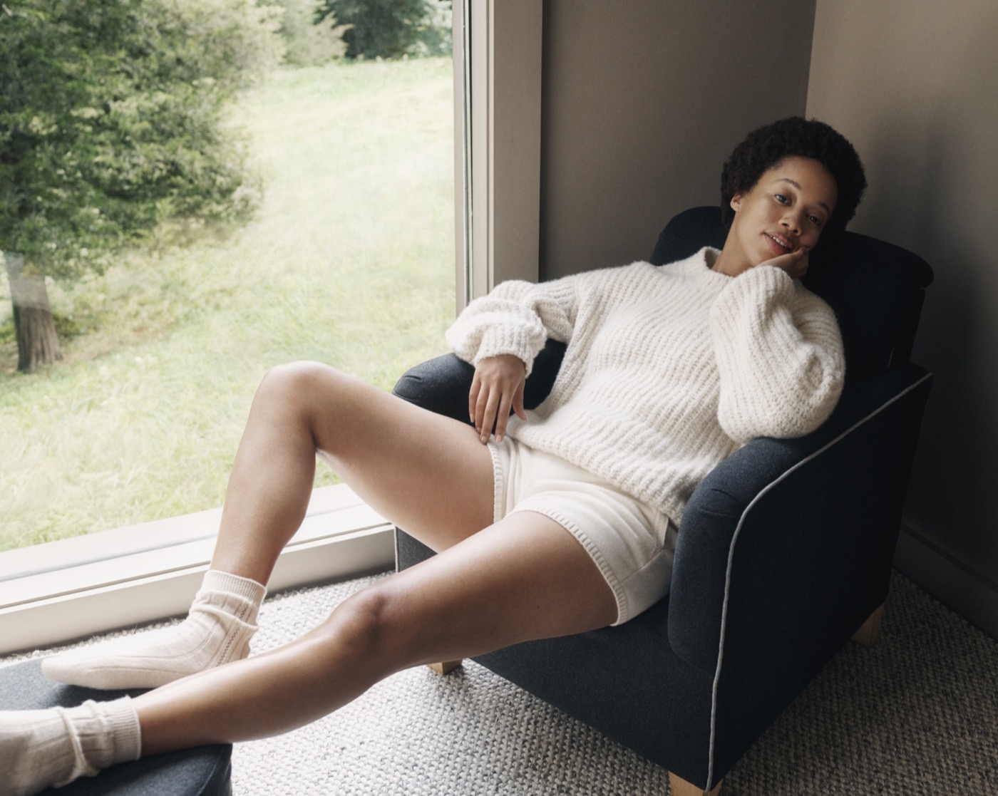 Lauren Ash resting in an armchair beside a sunlit window.