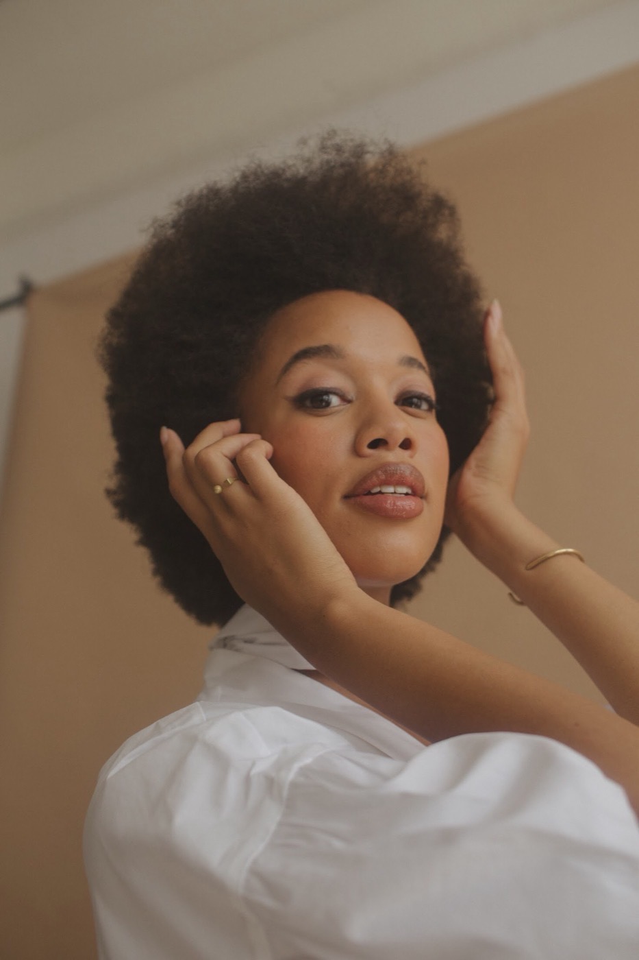 Close portrait of Lauren Ash in a white shirt, hands framing her face.