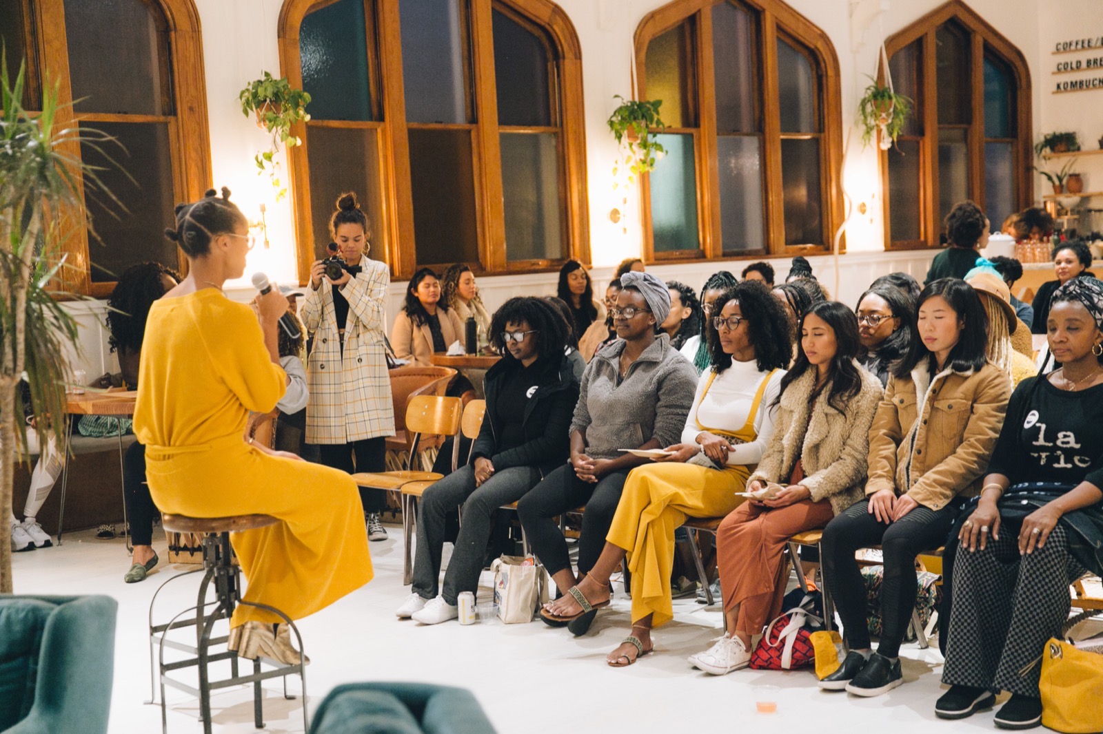 Lauren Ash speaking to a seated audience of women at an intimate community gathering.